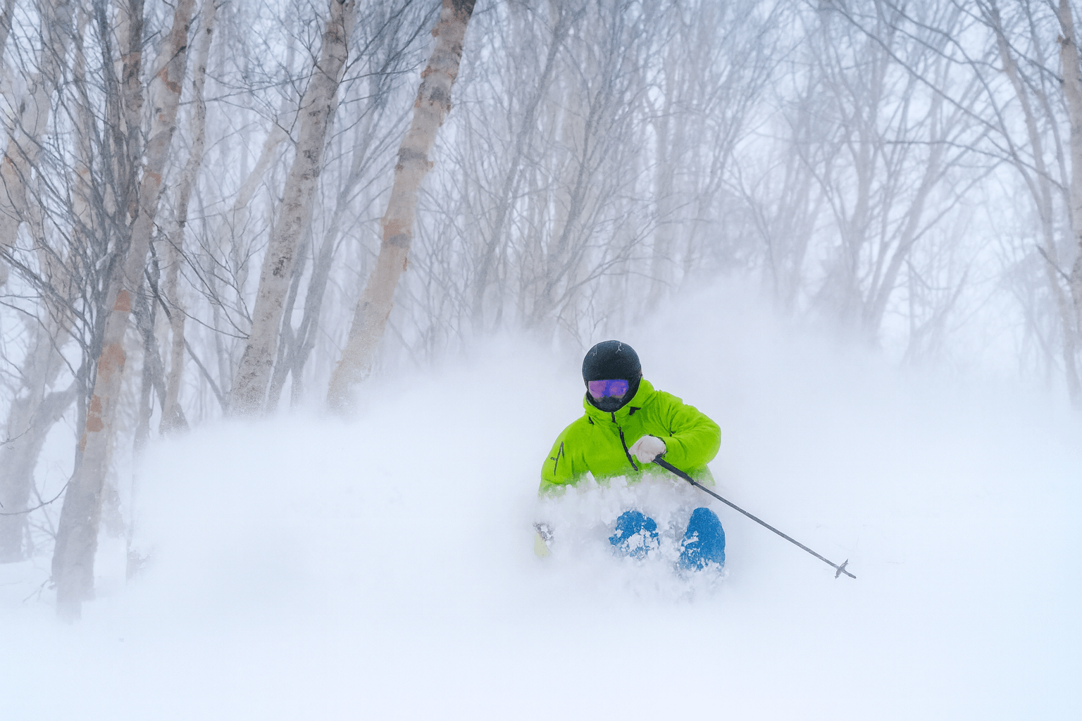 Skier in waist deep powder amongst the trees